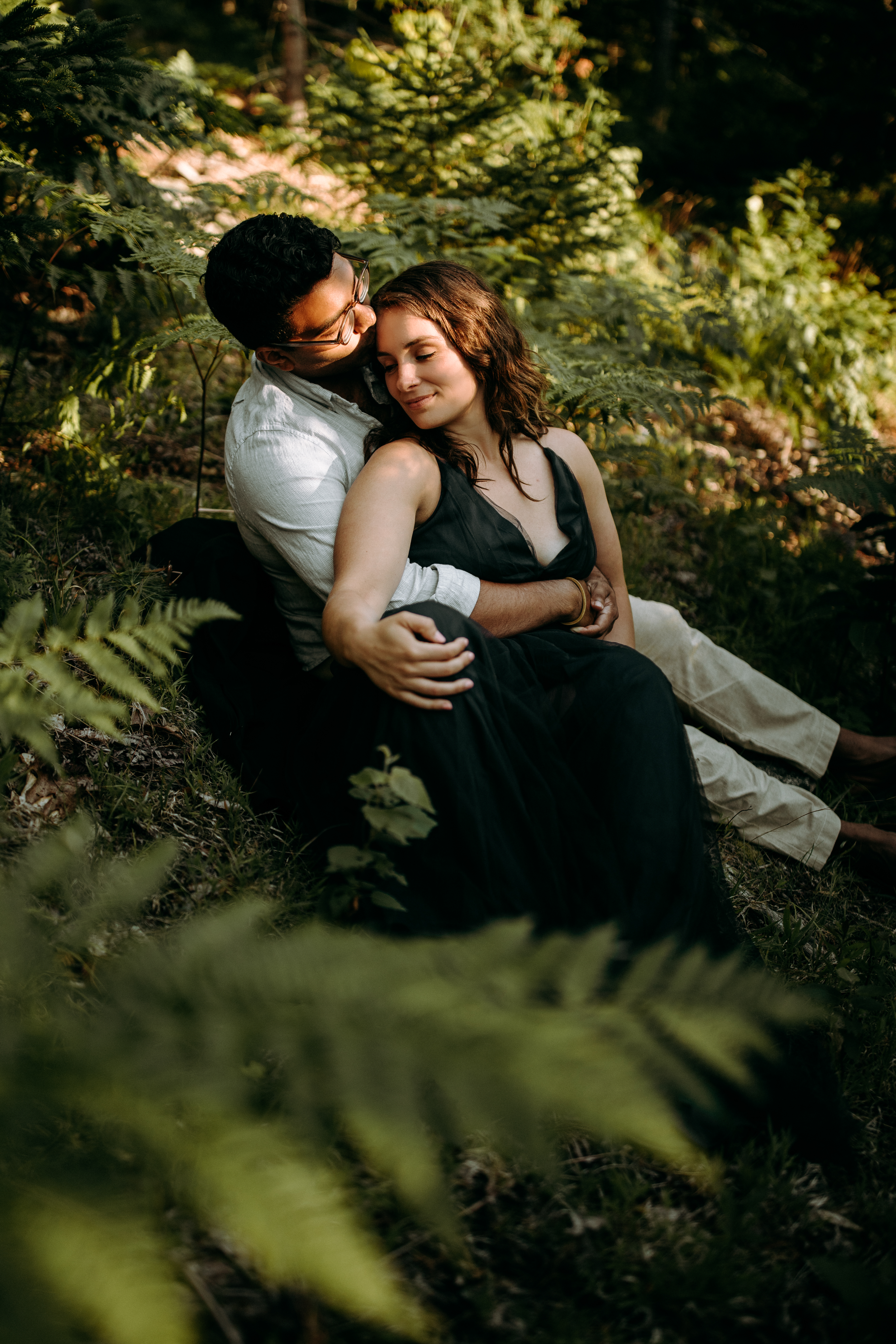Couple is snuggling in the forest with ferns surrounding them on Cadillac mountain in Acadia National Park