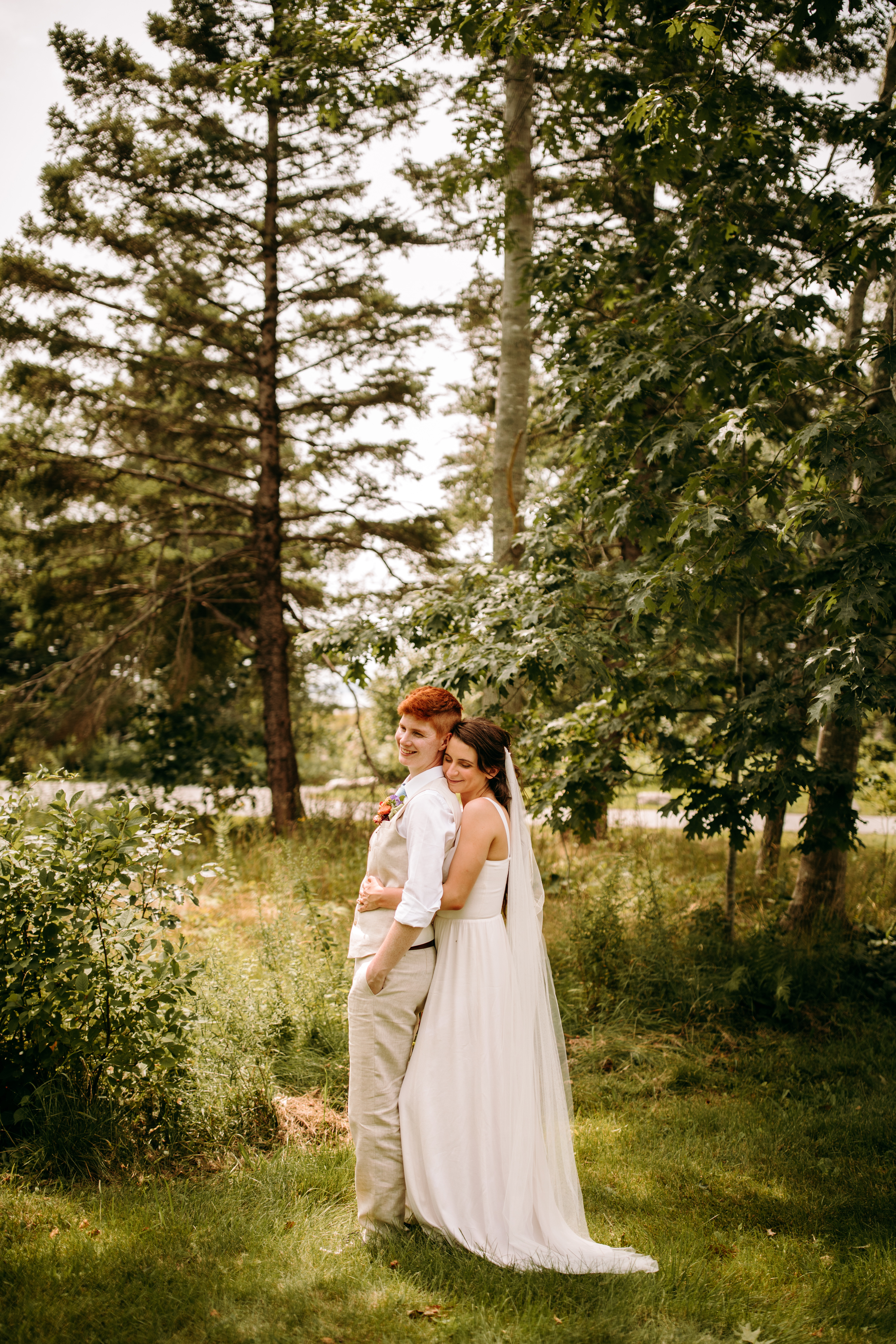 Lesbian LGBTQ Acadia Wedding photography woodsy couple standing under trees hugging at Acadia National Park picnic spot