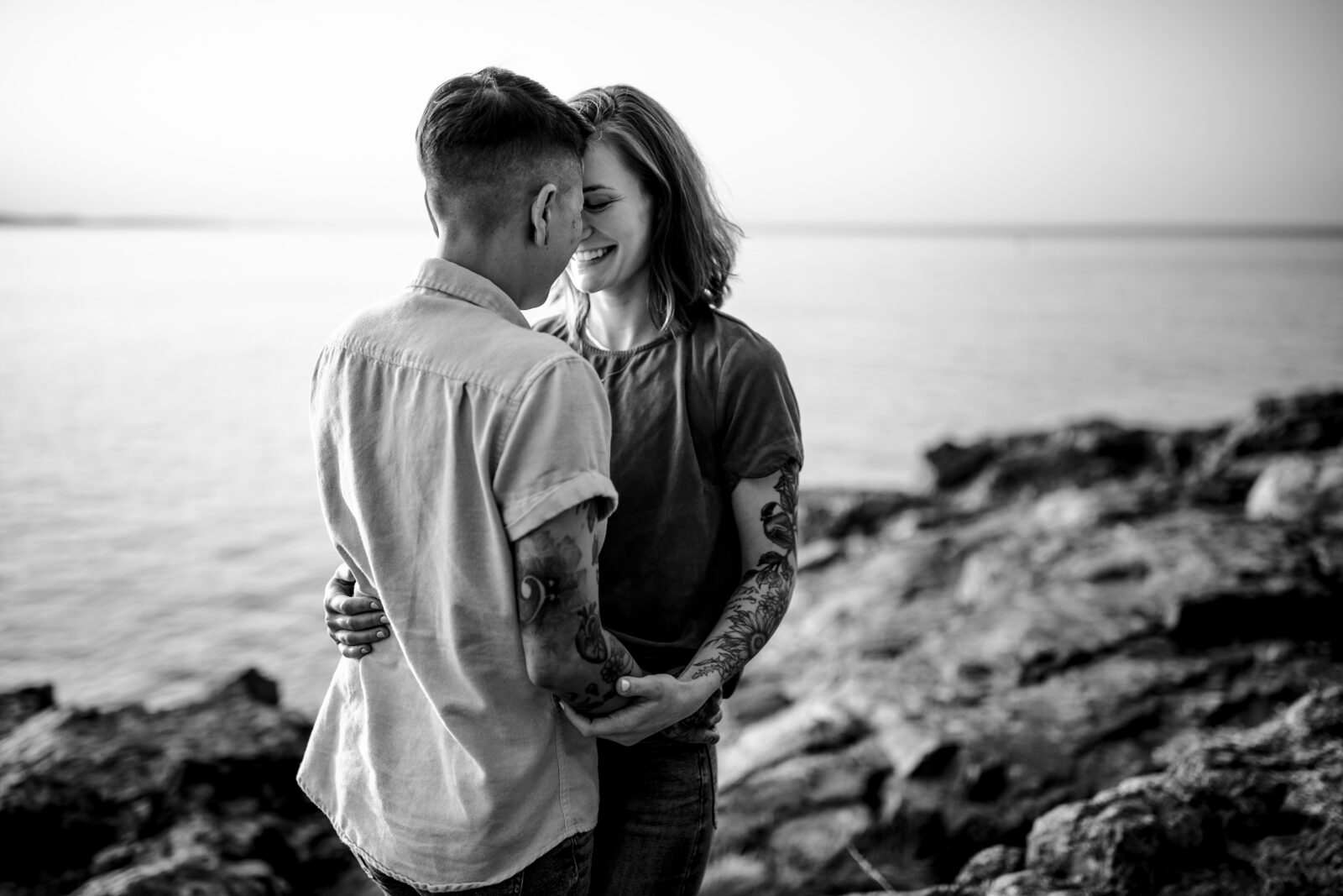 black and white photo of lesbian couple with the ocean and cliffs in the background
