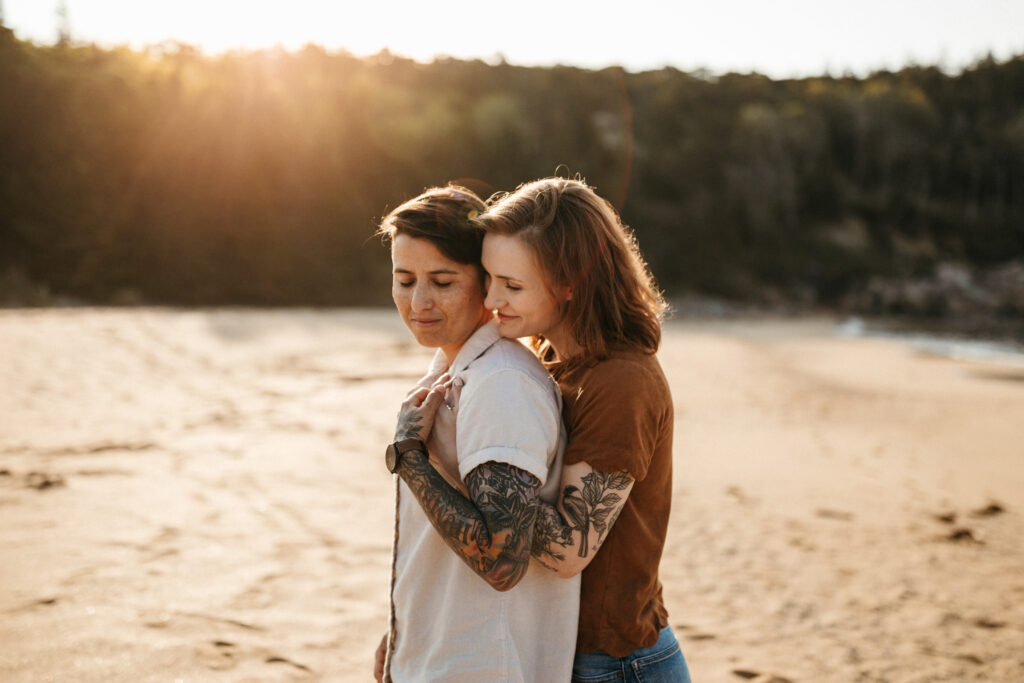 intimate hug of two women embracing on sand beach for sunrise in acadia national park 