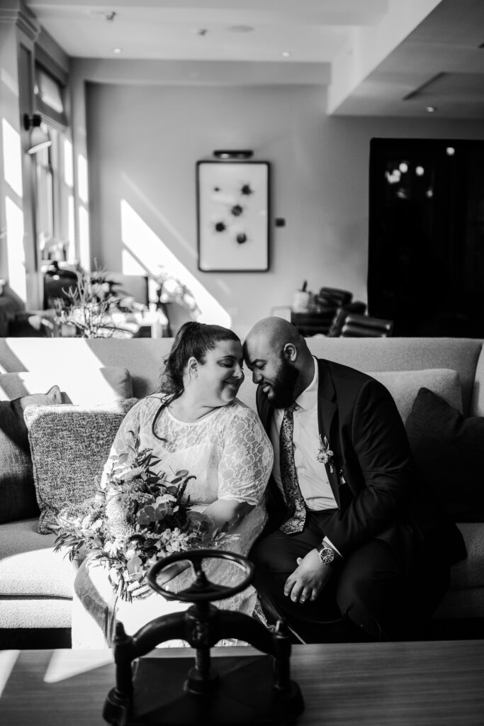 Bride and groom enjoying a quiet moment together in a cozy hotel room, with sunlight streaming in through the window