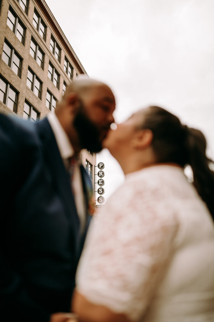 Creative photo of couple kissing after their Portland Maine city hall elopement with the press hotel in focus behind them 