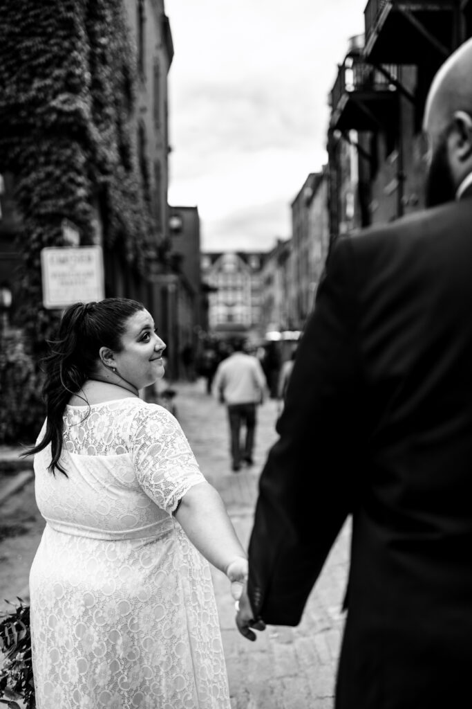 Bride looks back at groom on cobblestone streets in Portland Maine