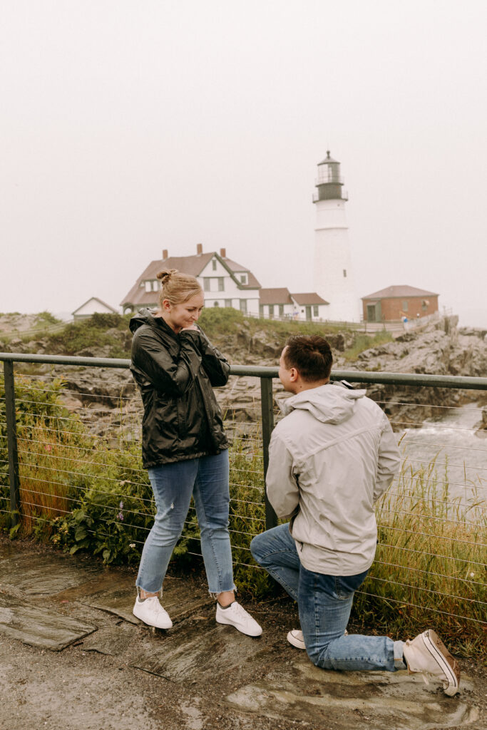Man kneels down and proposes to his girlfriend at the Portland Head Light