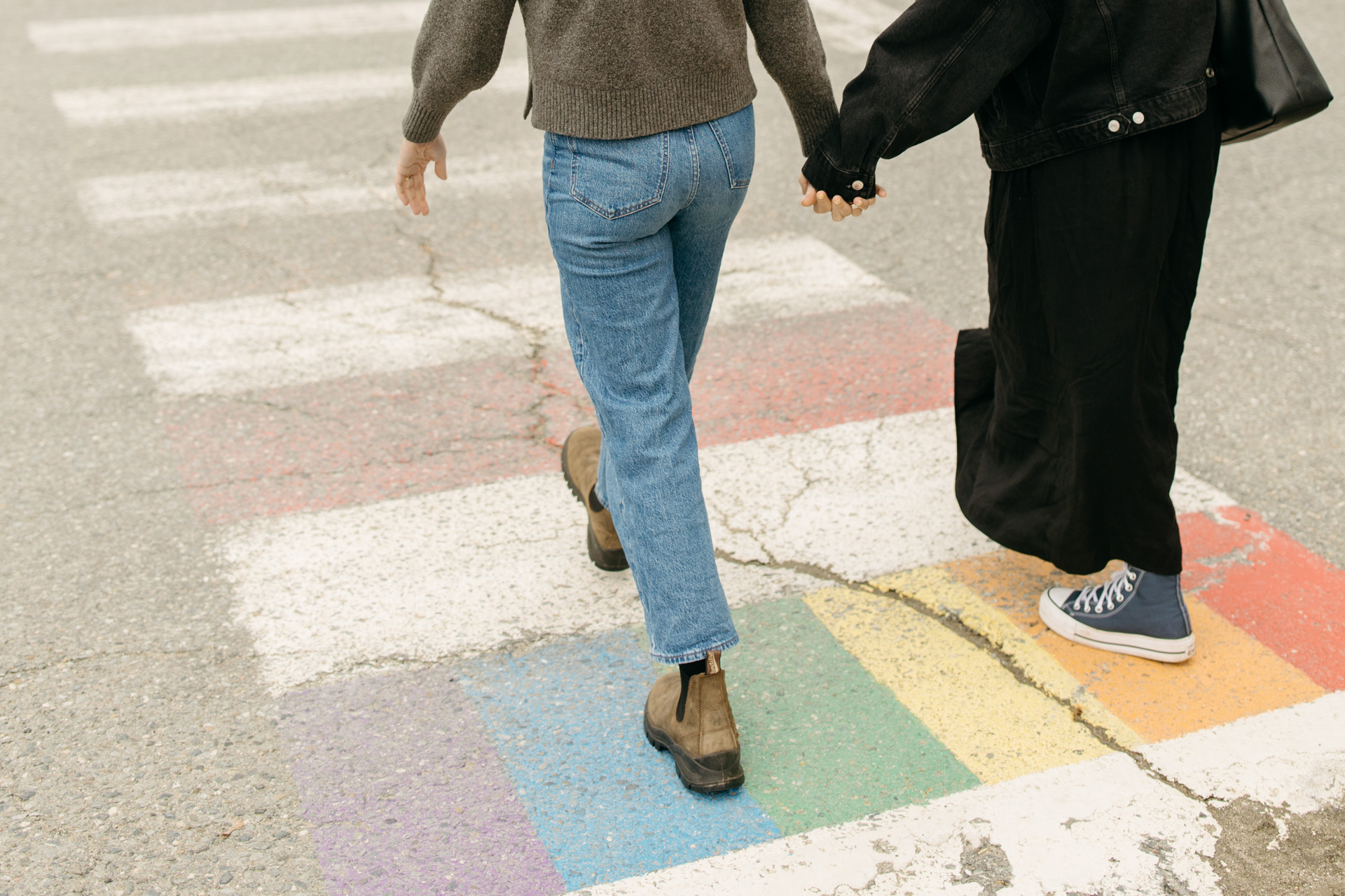 lesbian couple holding hands as they walk across a pride rainbow sidewalk