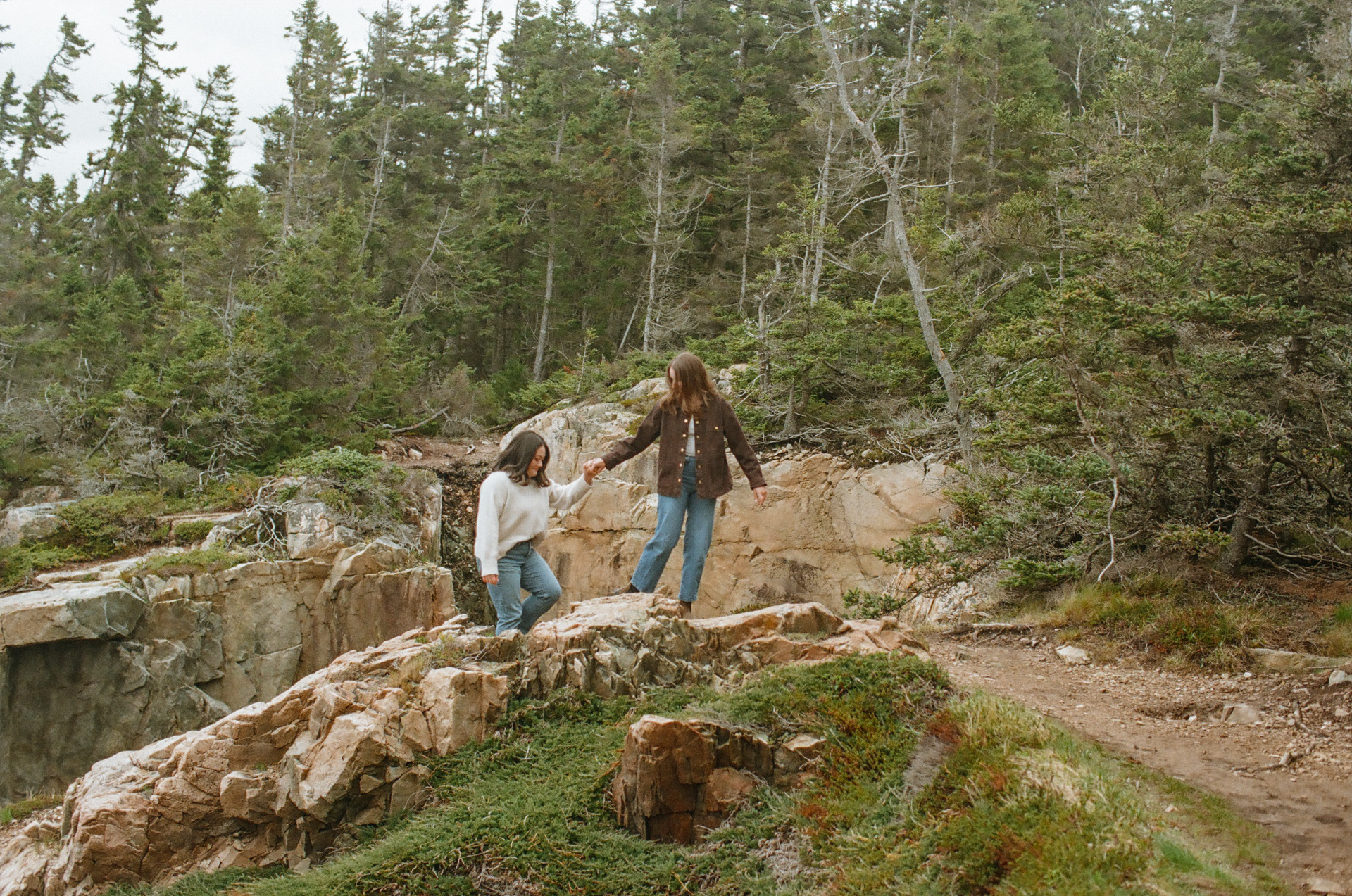 acadia engagement session photo on 35mm film grainy nostalgic. lesbian couple holding hands and walking across cliffside in Acadia national park Maine