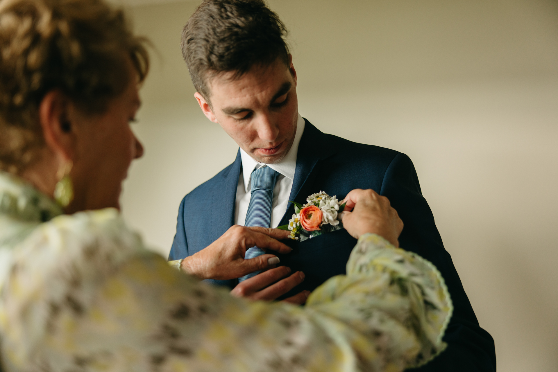 mother of groom helps put pocket boutonniere in the suit pocket before their wedding at the cliff house in york maine 