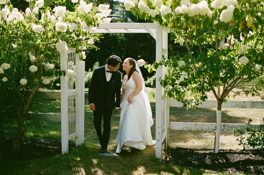 Maine wedding film photography, 35mm film photograph of couple walking through the gate at Live Well Farm with hydrangeas surrounding them 