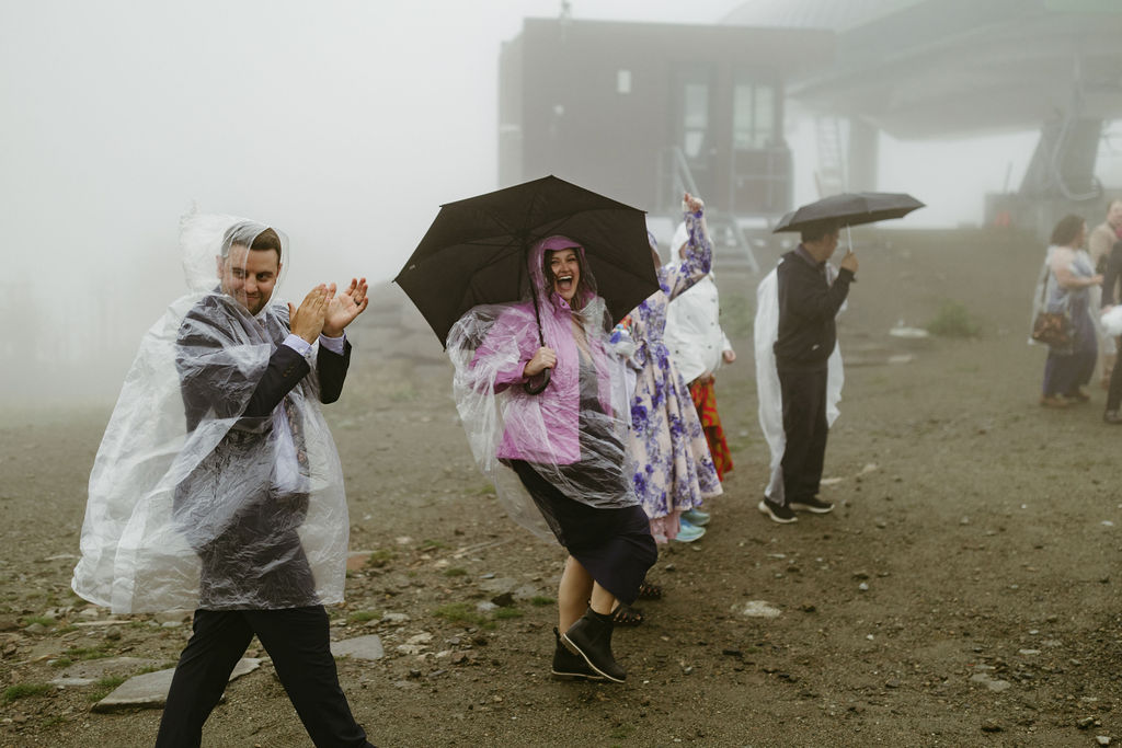 Wedding guests cheering at the camera in ponchos as they walk in the rain at Saddleback Mountain Wedding