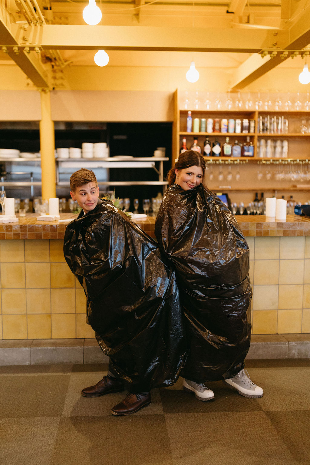 Brides in trash bags in a silly pose at The Nest before heading out to the ski lift at their wedding at Saddleback Mountain in Rangeley Maine 